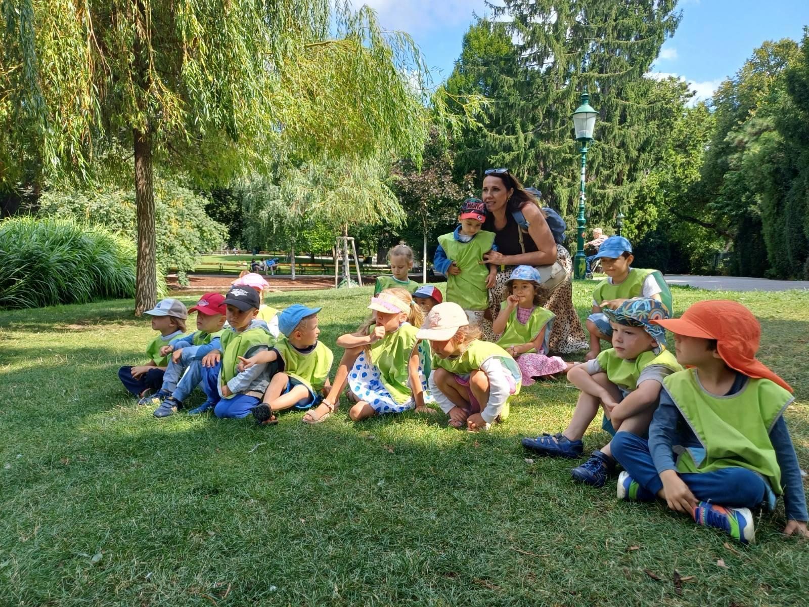 Kinder und eine Begleitperson sitzen gemeinsam auf einer Wiese im Park